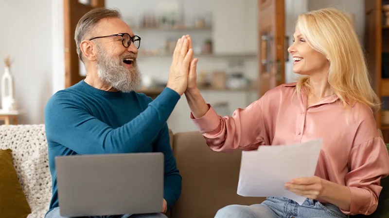 A husband and wife celebrate while finding a heat pump on a laptop