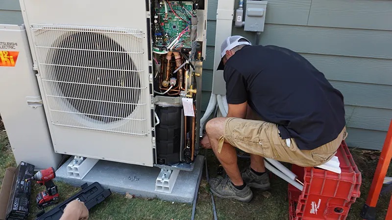 A Bill’s Heating employee works on installing a ductless heat pump condenser.