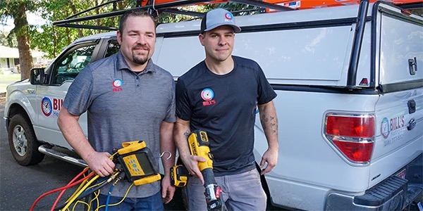 Two technicians walk toward a home with HVAC tools in hand